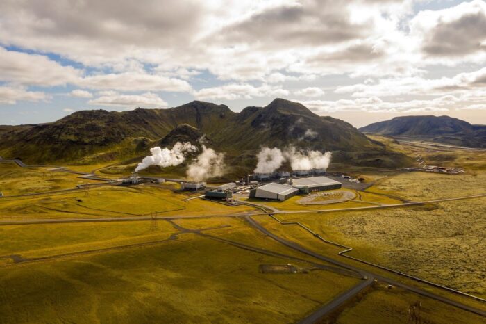 Geothermal power plant releasing steam beneath rugged volcanic mountains