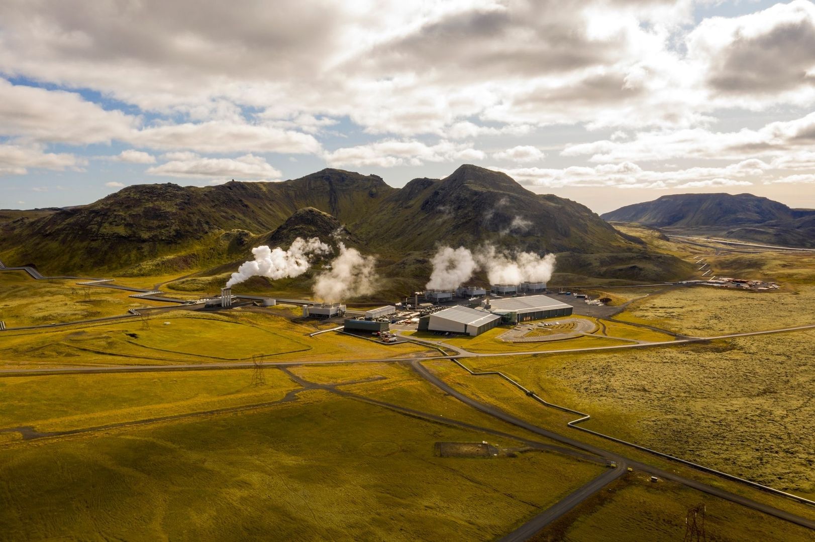 Geothermal power plant releasing steam beneath rugged volcanic mountains