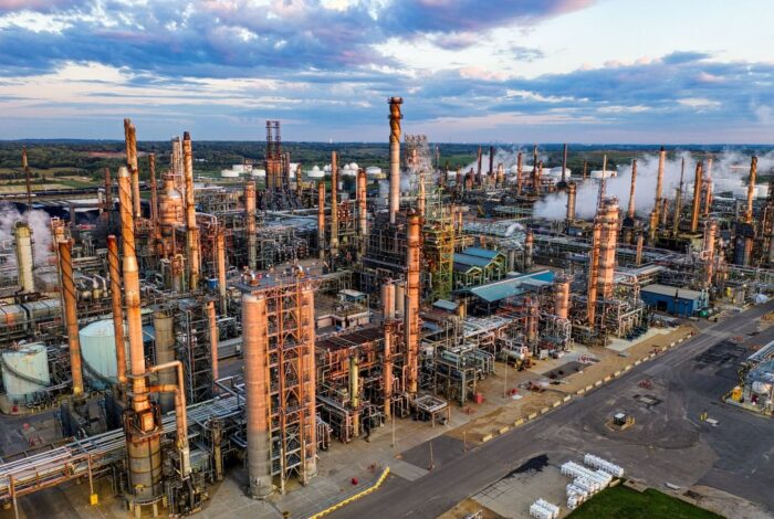 Aerial view of a sprawling industrial refinery with towers, pipes, and steam