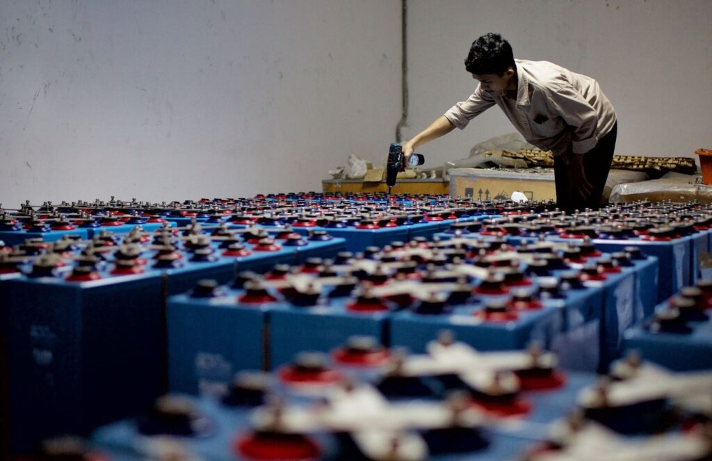 Worker assembling rows of large blue battery units in an indoor facility